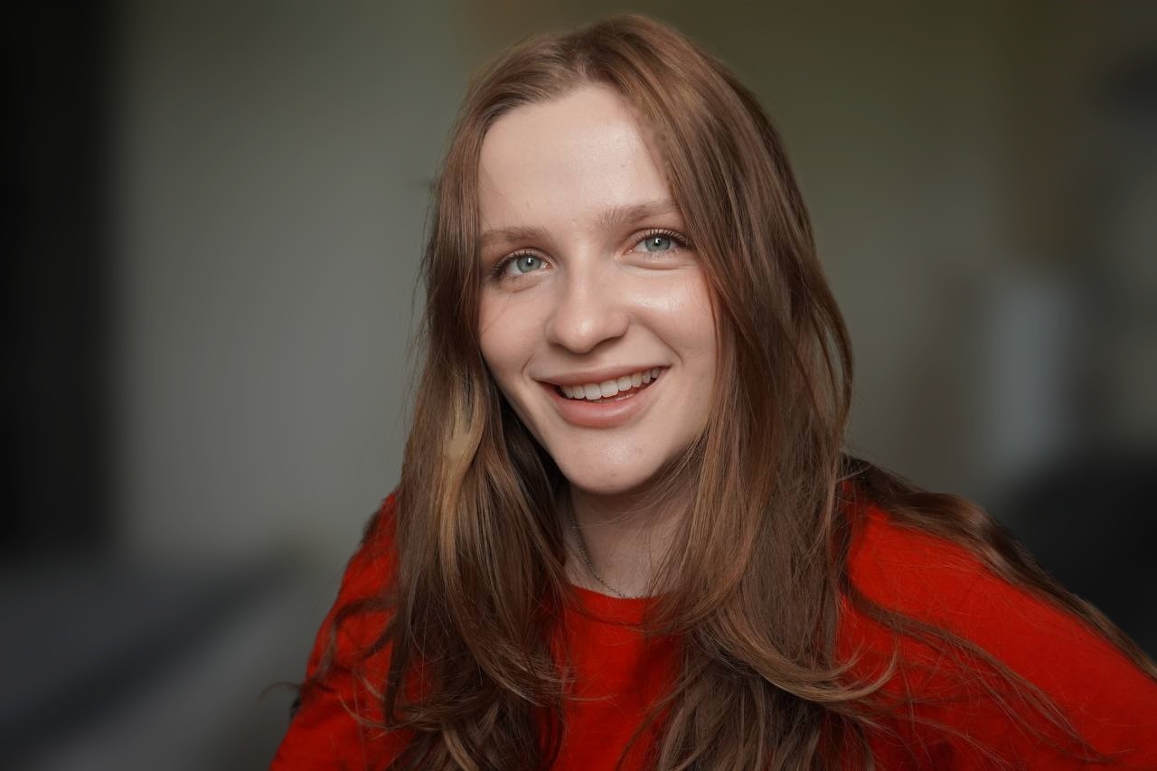 Vee, smiling, in a red sweater